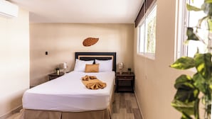 A bedroom with a bed, bedside tables, a wall-mounted leaf decoration, and a window with a view of greenery. - Hostal las Rosas de Punta Cana (Punta Cana)