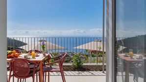 Varanda com mesa posta para o café da manhã, com vista para a costa, guarda-sóis e céu claro.