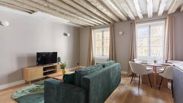 Una sala de estar moderna con un sofá, televisión, suelo de madera y un comedor con sillas y una mesa.