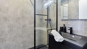 A modern bathroom with a glass-enclosed shower, a black sink with a soap dispenser, and a mirror above the sink. - Magnificent new Flat Le Marais/beaubourg (Paris)