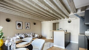 A dining area with a wooden table set for four, a sofa, and a kitchen in the background. - Charming new Flat Le Marais/beaubourg (Paris)