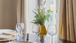 A dining area with a round table set for four, featuring woven placemats, clear glassware, and a yellow vase with greenery. - Charming new Flat Le Marais/beaubourg (Paris)