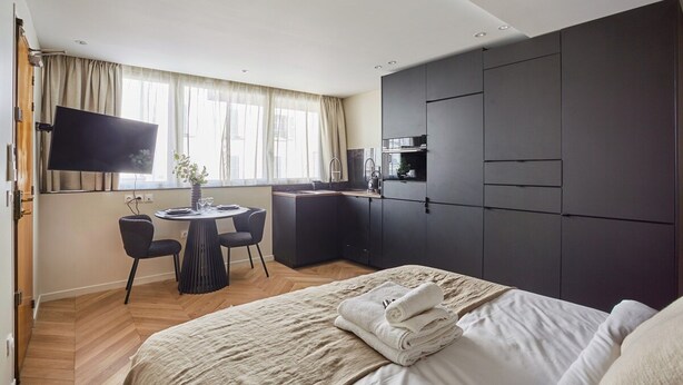 Una camera d'albergo moderna con un letto, una scrivania, una TV a schermo piatto e angolo cottura.