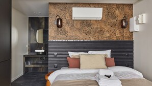 Camera d'albergo moderna con un letto grande, una doccia integrata e una parete testurizzata sopra il letto.