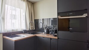 Una cucina moderna con un frigorifero nero, forno a incasso, lavello e una finestra con tende leggere.