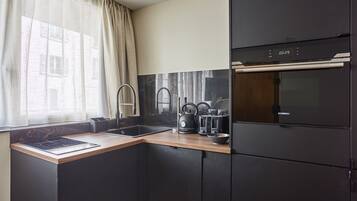 Een moderne keuken met een zwarte koelkast, een inbouwoven, een spoelbak en een raam met dunne gordijnen.