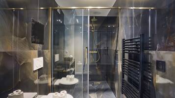 Een moderne badkamer met een douchecabine van glas, een zwarte handdoekhouder en twee toiletten met toiletpapier.