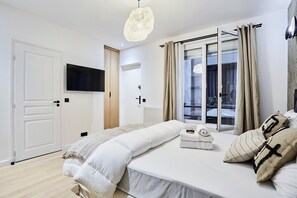 Ein Schlafzimmer mit Bett, einem an der Wand montierten Fernseher, einem Fenster mit Vorhängen und einer Tür.