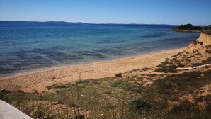 A beach with clear blue water, sandy shore, and a distant view of hills.