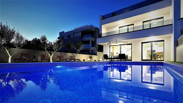 A modern residential building with a swimming pool, outdoor seating, and a well-lit entrance.