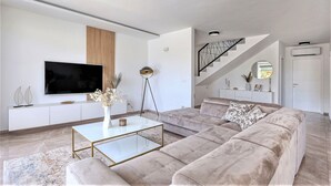 A modern living room with a large flat-screen TV, a sofa, a coffee table, and a staircase leading to an upper floor.