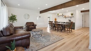 A spacious living room with a leather sofa, a coffee table, and a dining area with wooden chairs. - Big Groups~Game Room~5Bedroom~Kids Toys~Office (Des Moines)