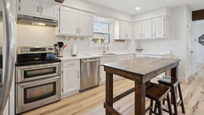 A modern kitchen with white cabinetry, stainless steel appliances, and a wooden island with stools. - Big Groups~Game Room~5Bedroom~Kids Toys~Office (Des Moines)