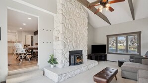 A living room with a stone fireplace, a television, and a large window. - Big Groups~Game Room~5Bedroom~Kids Toys~Office (Des Moines)
