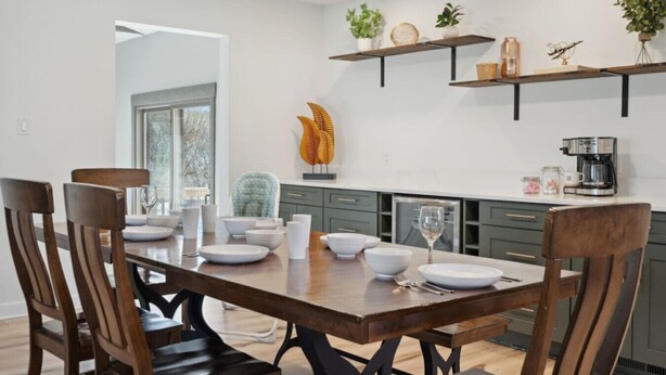 A modern kitchen with a wooden dining table, chairs, and built-in shelves with plants and kitchenware. - Big Groups~Game Room~5Bedroom~Kids Toys~Office (Des Moines)