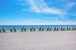 Una playa con hileras de sillas de descanso verdes y sombrillas.
