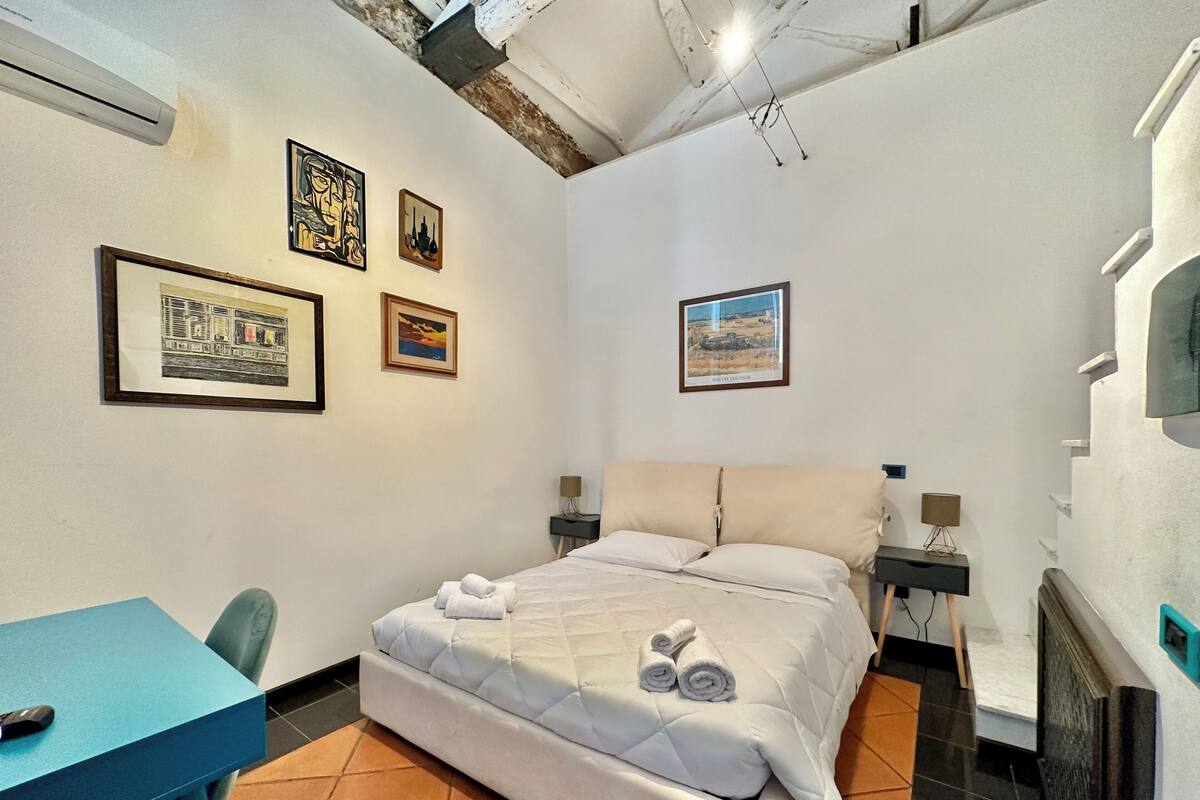 Een slaapkamer met een bed, een bureau en een stoel. Er hangen ingelijste foto’s aan de muur.