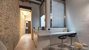 A modern kitchen with a brick wall, a window with blinds, and a bar area with stools.
