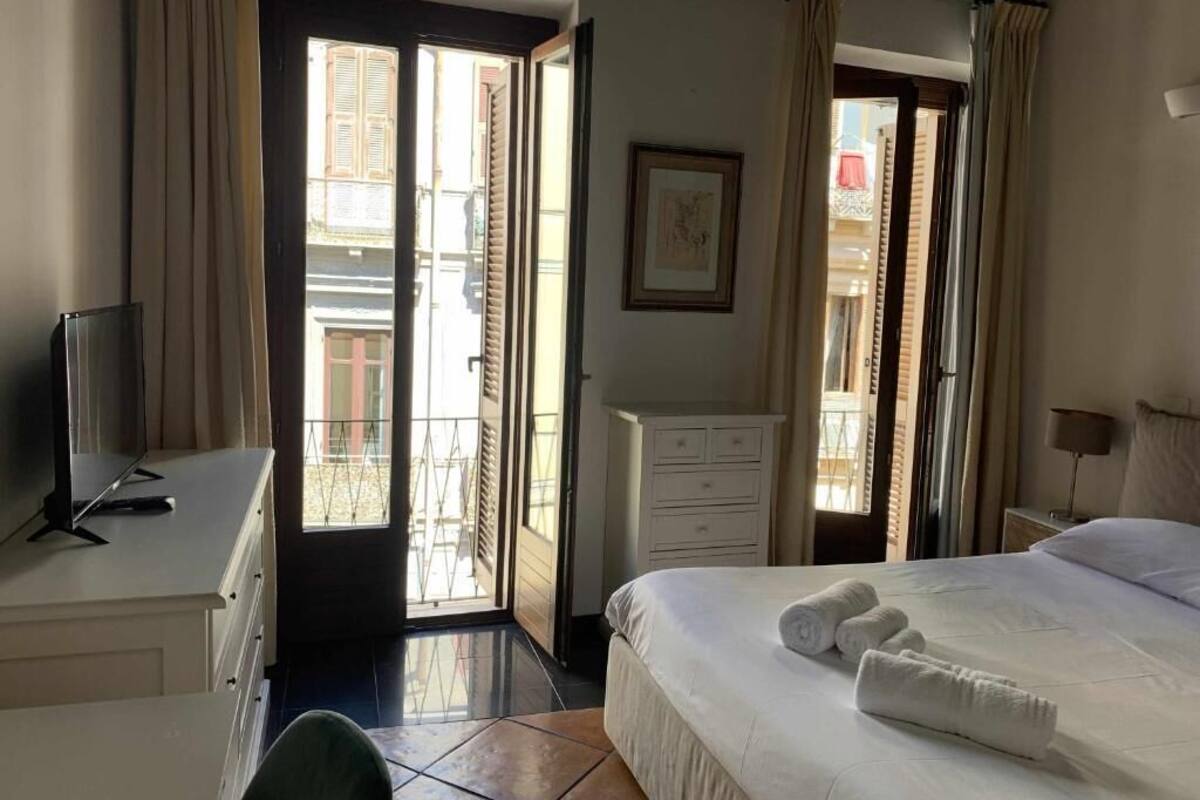 Hotelkamer met een bed, bureau met computer, een kast, raam met gordijnen en een deur naar een buitenruimte.