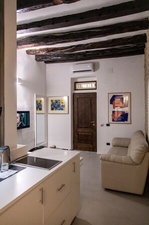 A modern room with a kitchenette, a wooden door, and artwork on the walls. - C&O Savoia Deluxe Rooms (Cagliari)