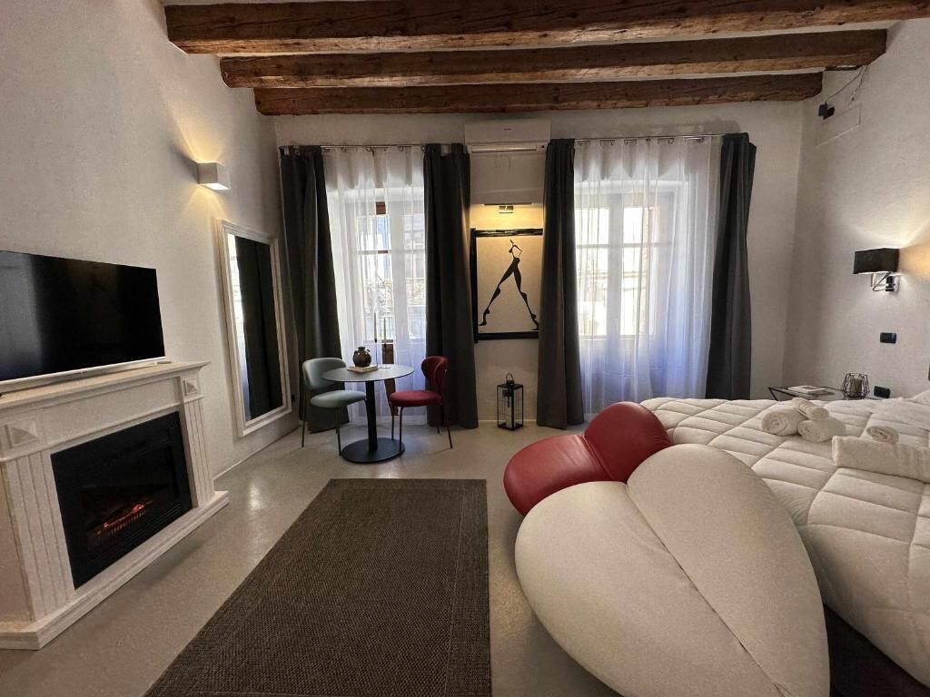 Ein modernes Hotelzimmer mit Kamin, einem großen Bett, einer Essecke mit Tisch und Stühlen sowie einem an der Wand montierten Fernseher.