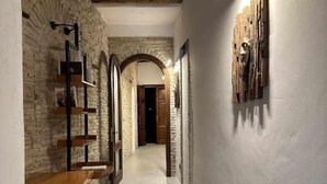 A hallway with exposed brick walls, wooden beams, a wooden bench, and a wooden door at the end.