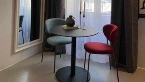 A room with a round table, two chairs, a vase, candles, and a window with curtains.