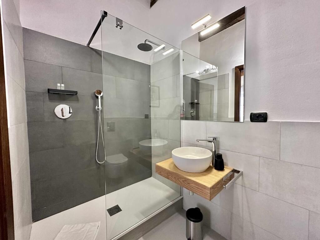 Ein modernes Badezimmer mit einer gläsernen Duschkabine, einem weißen Waschbecken und einem Spiegel darüber.
