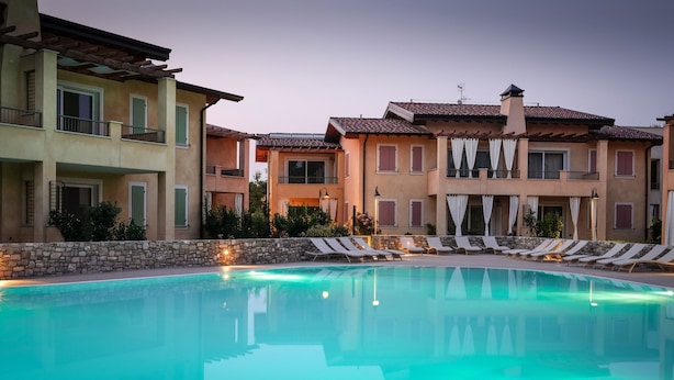 A poolside view of a hotel with multiple buildings, a stone wall, and lounge chairs. - Le Corti Caterina C3 by Wonderful Italy (Lonato del Garda)