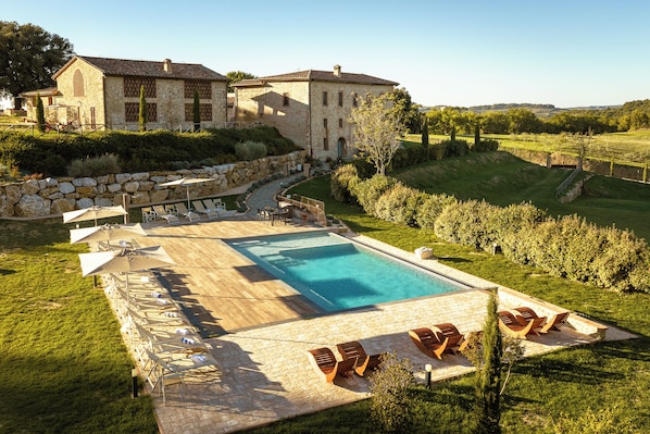 A large stone building with a swimming pool, surrounded by a well-maintained lawn and a vineyard.