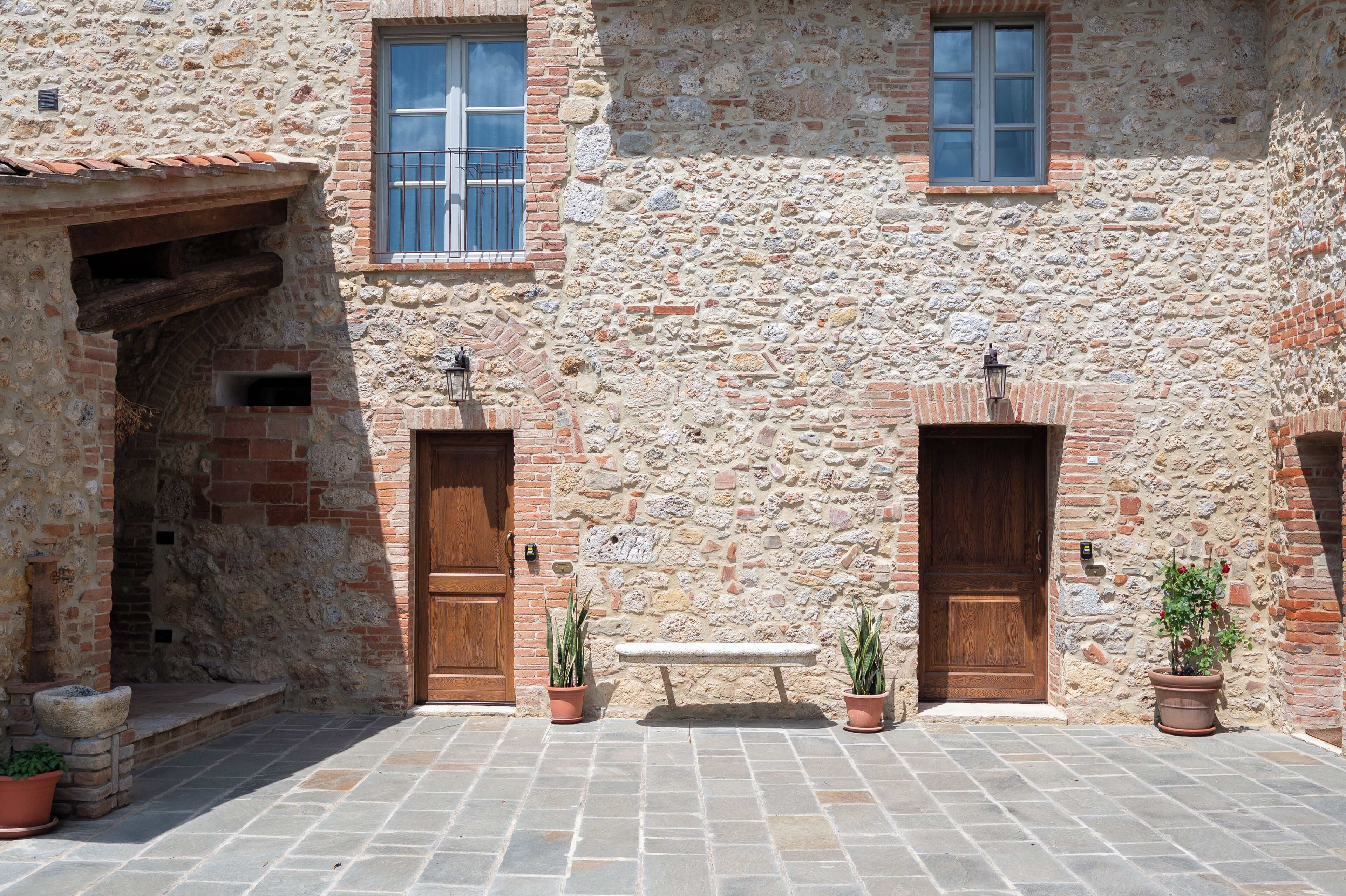 A courtyard with stone walls, wooden doors, and potted plants.