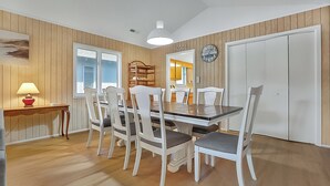 A dining area with a wooden table and white chairs, a lamp, and a clock on the wall.