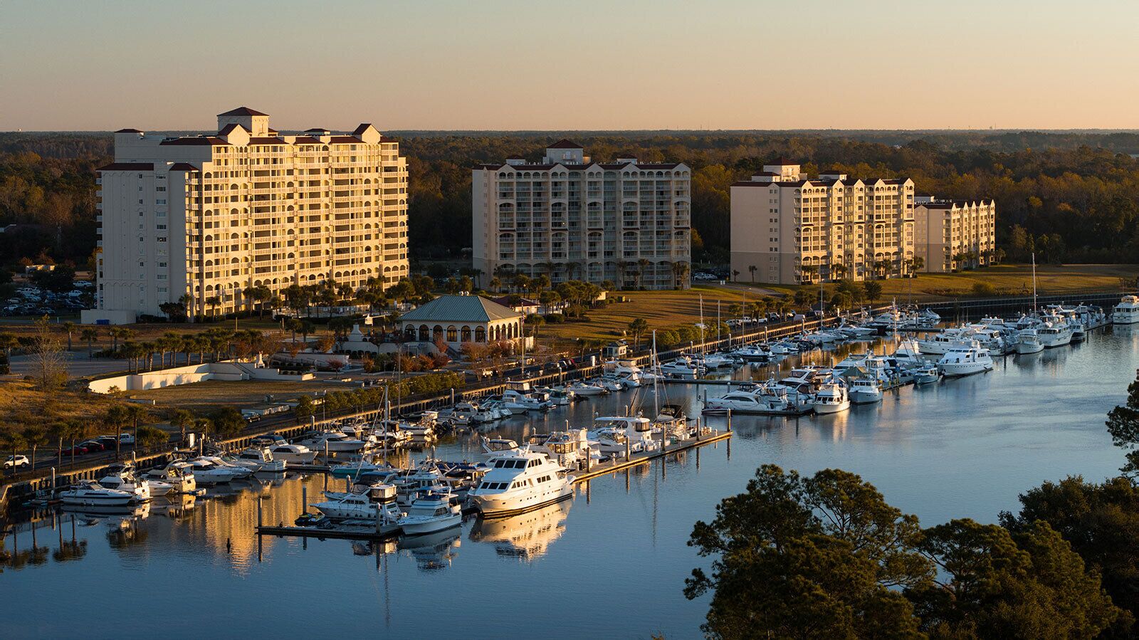 A marina with multiple boats docked, surrounded by high-rise buildings and a clear sky.