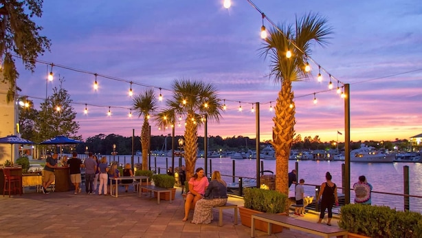 An outdoor dining area with string lights, palm trees, and a view of the marina.