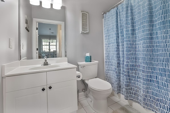 Un baño con lavamanos blanco, inodoro y cortina de ducha con estampado azul.
