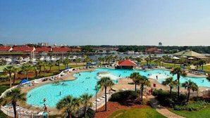 A large outdoor swimming pool surrounded by palm trees and lounge chairs, with a view of a cityscape in the background.