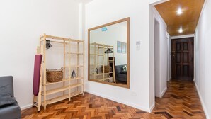 A hallway with a wooden herringbone floor, a large mirror, a wooden shelf unit, and a grey sofa. - Pi502 Zona4 in Rio de Janeiro (Rio de Janeiro)