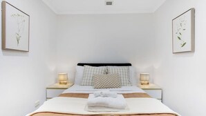 Une chambre à coucher bien rangée, avec un lit, deux tables de chevet et deux lampes fixées au mur.