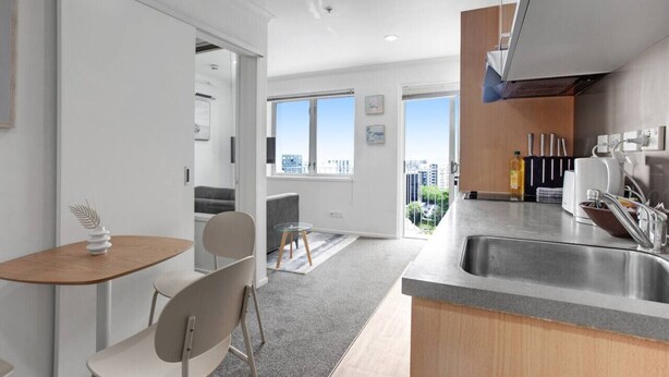 Une cuisine moderne dotée d’une grande fenêtre, un coin repas avec une table et des chaises, et une vue sur le paysage urbain.