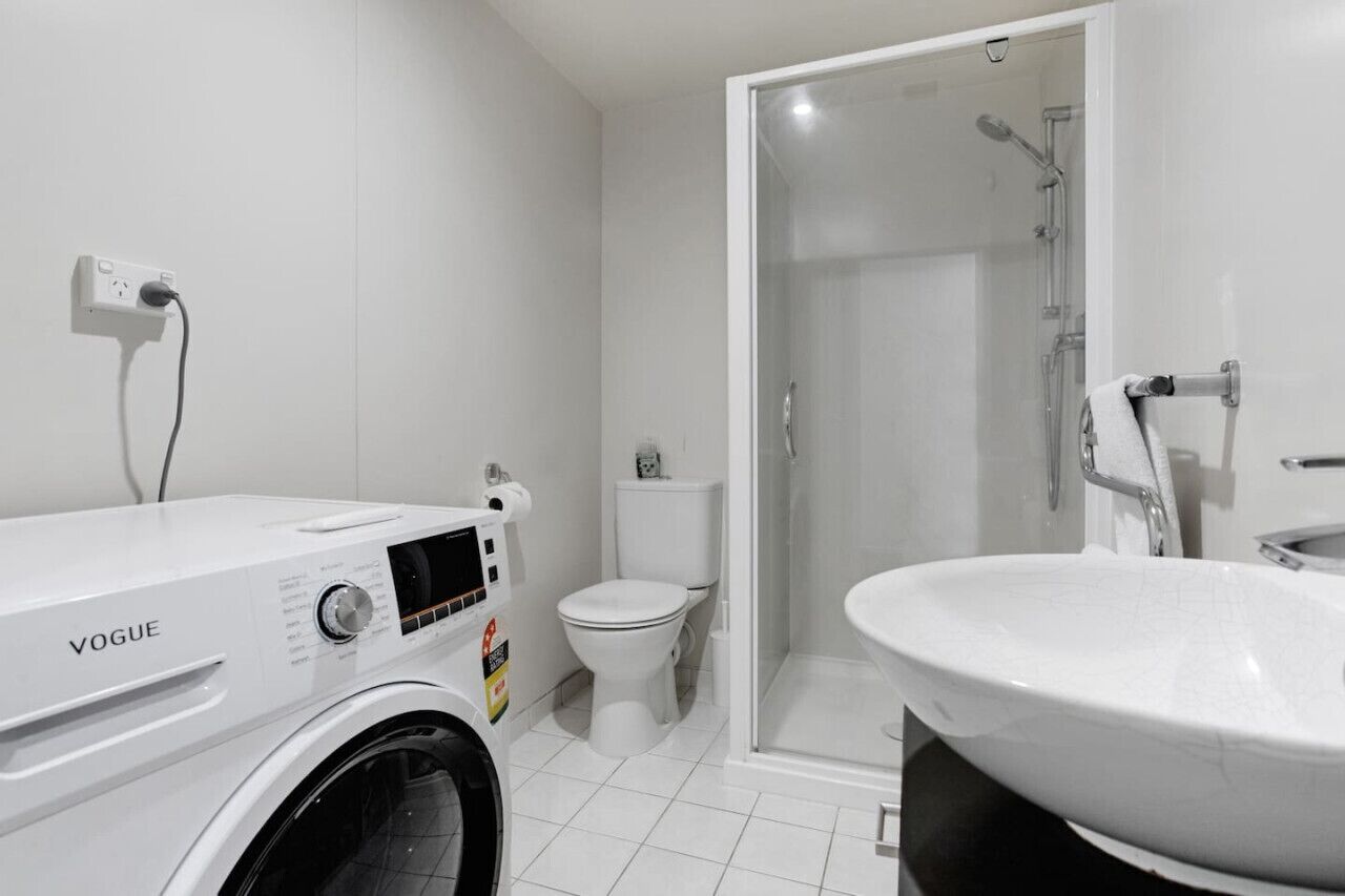 Une salle de bain moderne équipée d’un lave-linge, de toilettes et d’une douche.