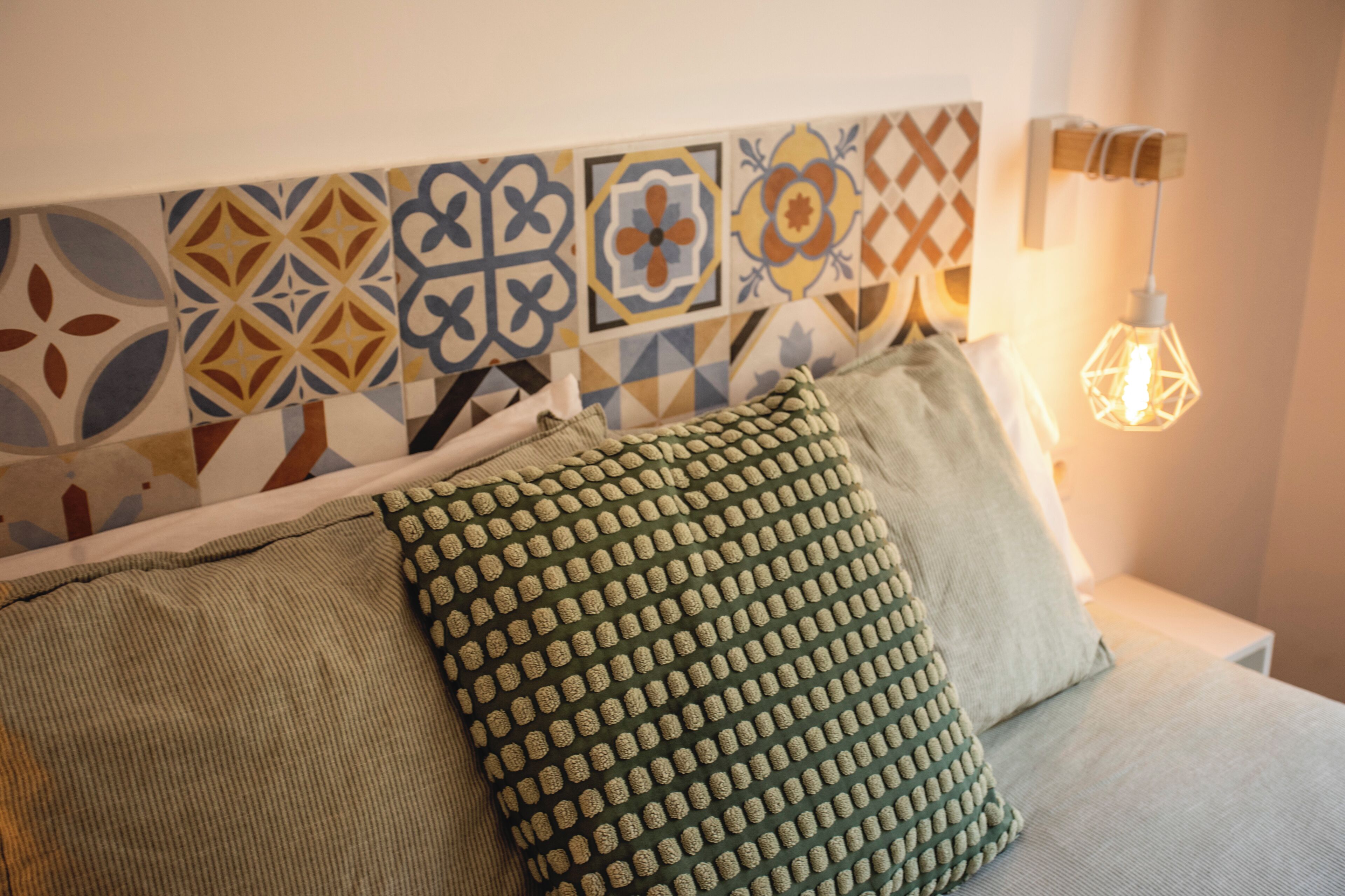 Una cama con almohadones estampados, un diseño geométrico en la pared y una lámpara colgante.