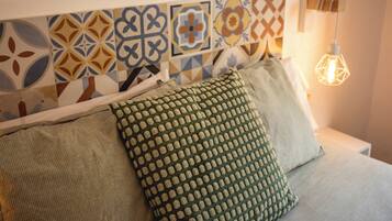 Una cama con almohadones estampados, un diseño geométrico en la pared y una lámpara colgante.
