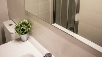 A bathroom with a white sink, a potted plant, a mirror, and a shower enclosure.