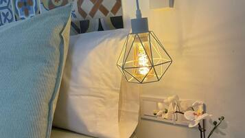 A neatly arranged bedroom with a bed, a bedside table with a potted plant, a wall-mounted light fixture, and a decorative wall panel.