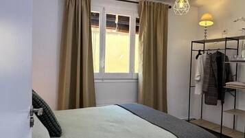 Een slaapkamer met een bed, een raam met gordijnen, een nachtkastje, een lamp en een kledingrek.