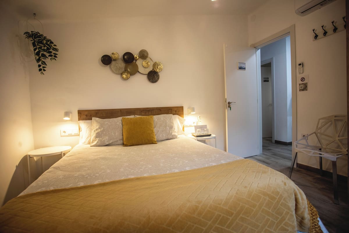 A neatly arranged bedroom with a large bed, bedside tables, a wall-mounted clock, and a door leading to another room.