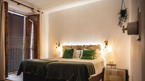 Una cama doble con ropa de cama verde y blanca, una mesita de noche con dos velas y una silla con cojín estampado.