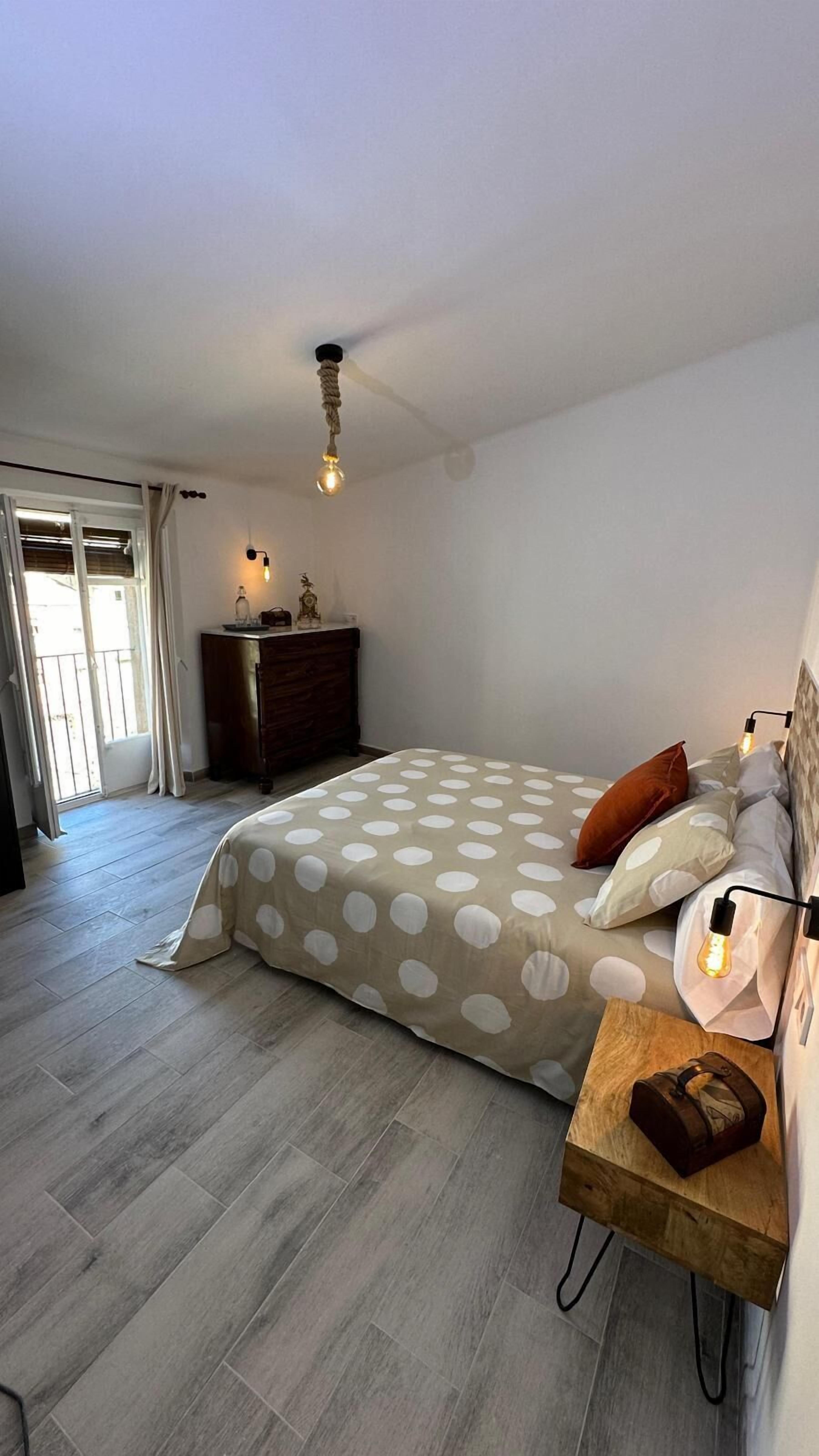 A bedroom with a bed, a wooden nightstand, a dresser, and a ceiling light fixture.