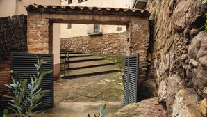 Una escalera de piedra que conduce a una entrada cubierta con persianas metálicas, rodeada de paredes de piedra rústica y un pequeño balcón.