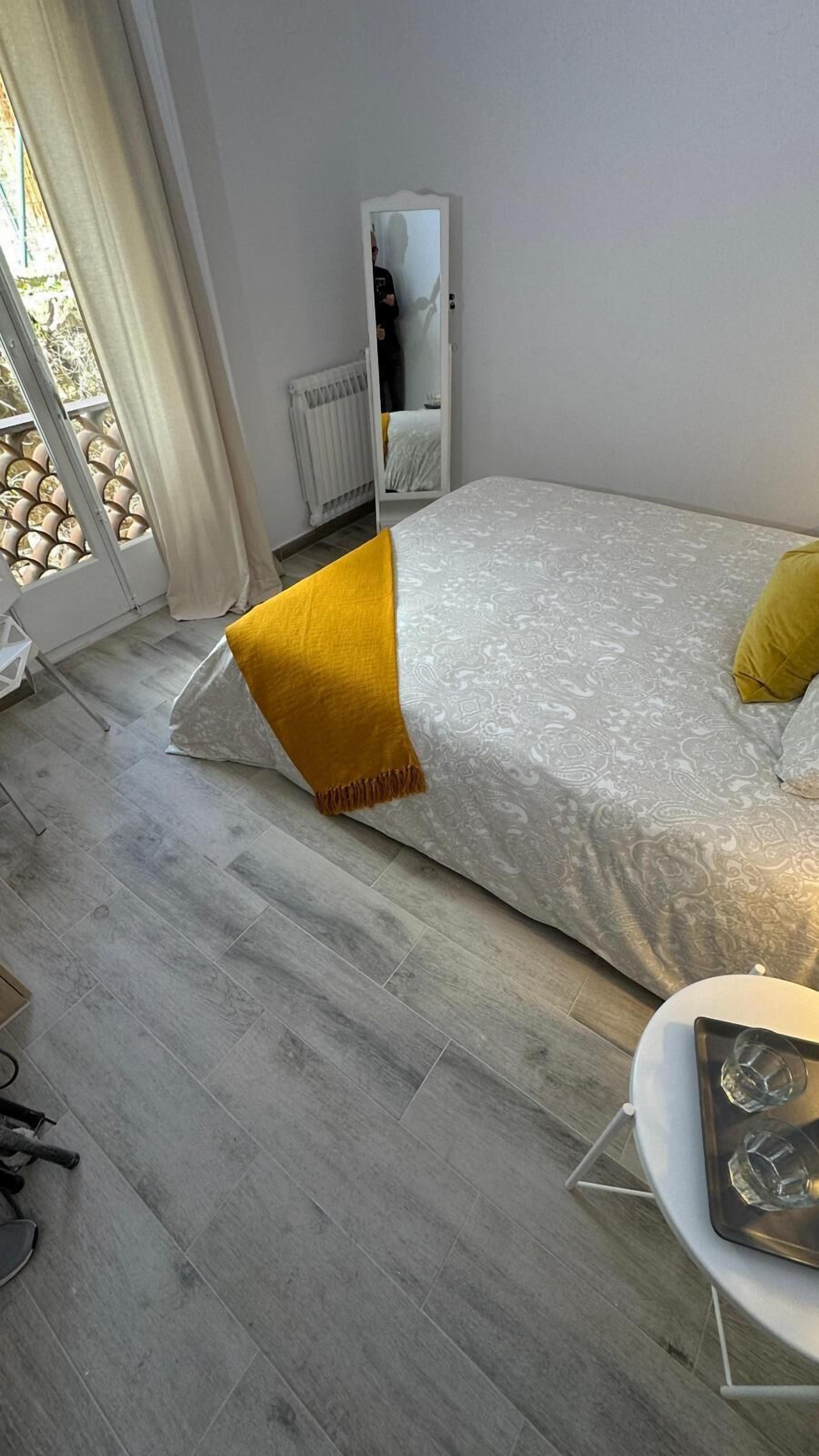 Ein Schlafzimmer mit Bett, Spiegel, Heizkörper und einem Fenster mit Vorhängen.